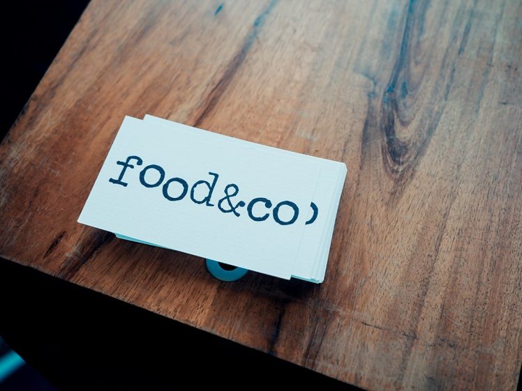 Image of A stack of business cards with the words food&co printed in black lowercase letters rests on a wooden surface.