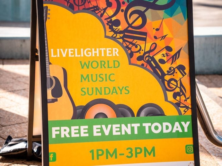 Image of A colourful sign advertises Livelighter World Music Sundays, a free event at Mandurah Performing Arts Centre from 1 pm to 3 pm. The sign features musical notes, a guitar, and the event website.