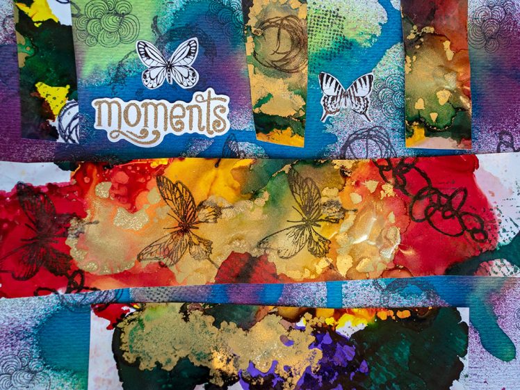 Image of A vibrant, abstract collage featuring colourful watercolour splashes, butterfly illustrations, and the word Moments in stylised text. The composition mixes reds, blues, greens, and yellows with layered textures.
