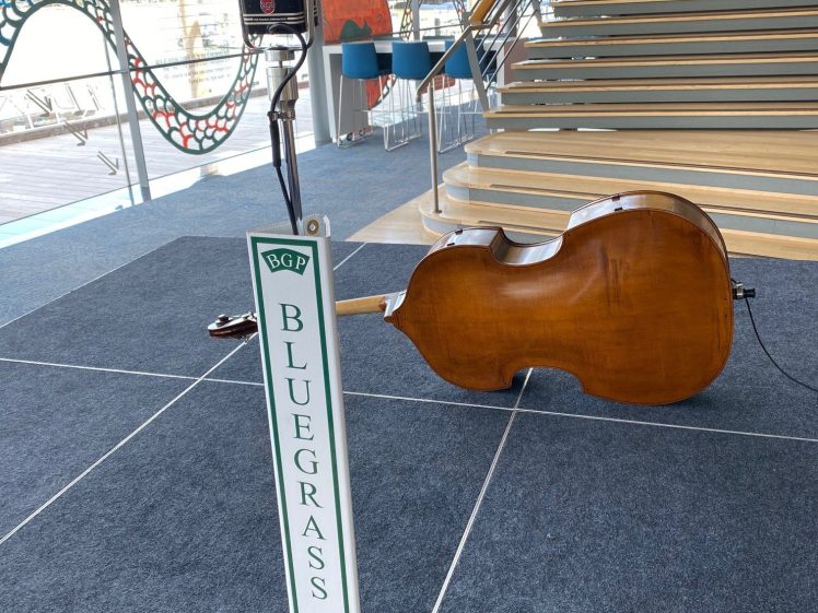Image of A double bass rests on its side beside a microphone and a Bluegrass Parkway sign on a stage with carpeted steps and a decorative wavy railing in the background.