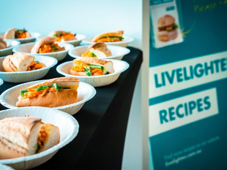 Image of Several plates with fresh sandwiches are arranged on a black table next to a sign that reads Livelighter Recipes with an image of a sandwich and some text partially visible.
