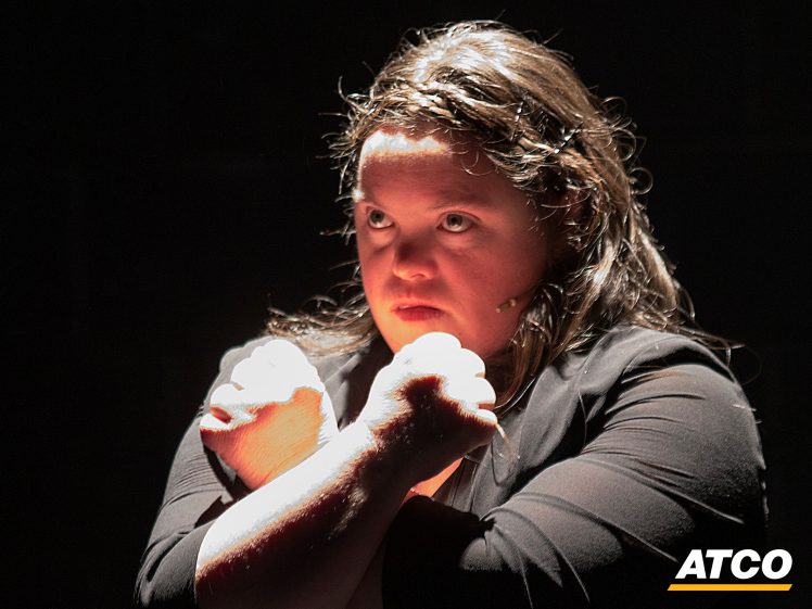 Image of A person with long hair and a serious expression stands in dramatic lighting, crossing their arms in front of their chest. The ATCO logo appears in the lower right corner.