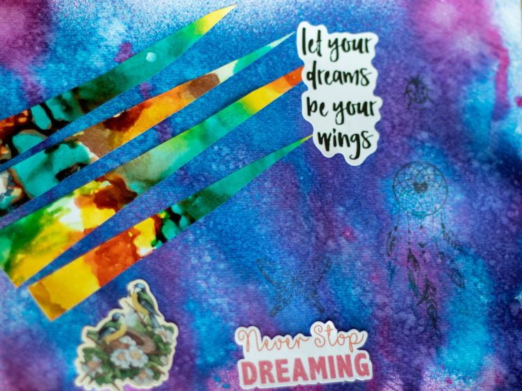 Image of A colourful, abstract background with watercolour textures in blue, purple, and pink. It features cut-out text saying let your dreams be your wings and Never Stop DREAMING, with dreamcatcher and floral stickers.