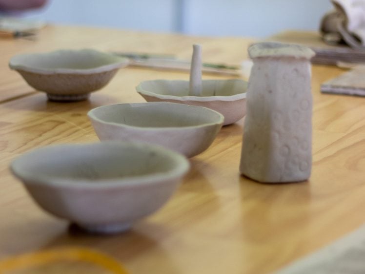Image of Unfinished ceramic bowls and a small vase sit on a wooden table, showcasing handmade pottery with rough, unglazed surfaces and unique shapes.