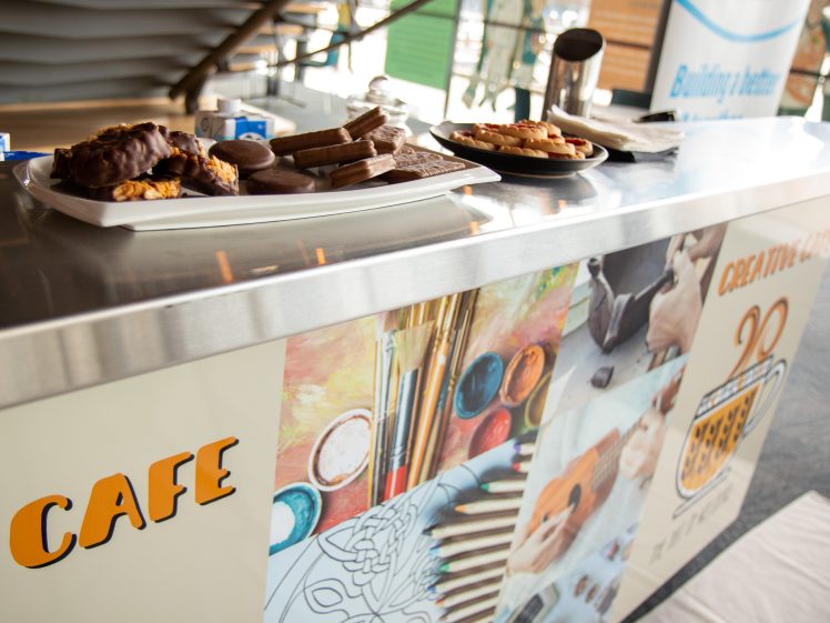 Image of A café counter displays assorted biscuits and chocolate-covered treats on plates. The counter is decorated with colourful art-themed graphics, including paintbrushes and musical instruments.