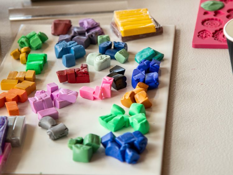 Image of Various small, colourful clay pieces are arranged on a white board, surrounded by art tools and moulds on a tabletop workspace.