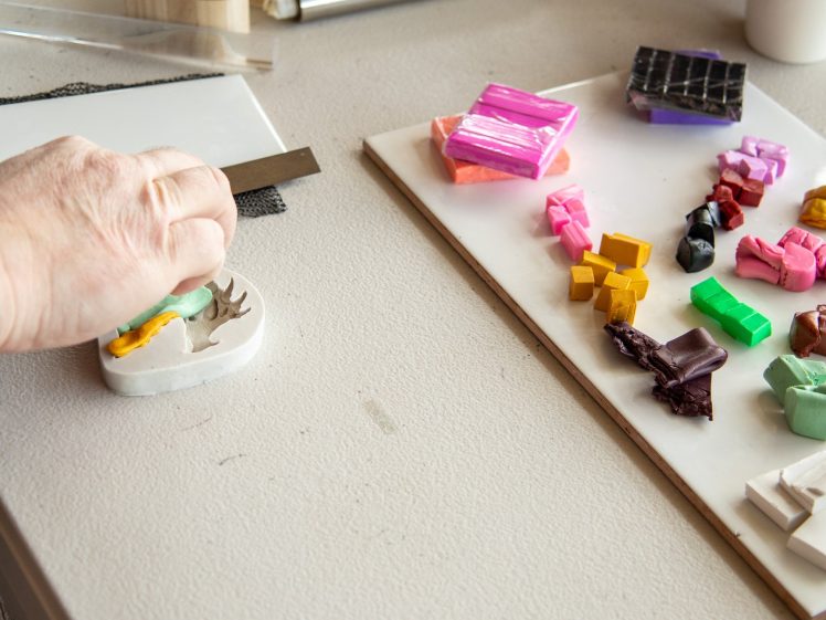 Image of A person presses coloured clay into a mould with one hand. Nearby, a tray holds various small blocks of colourful clay on a light tabletop.