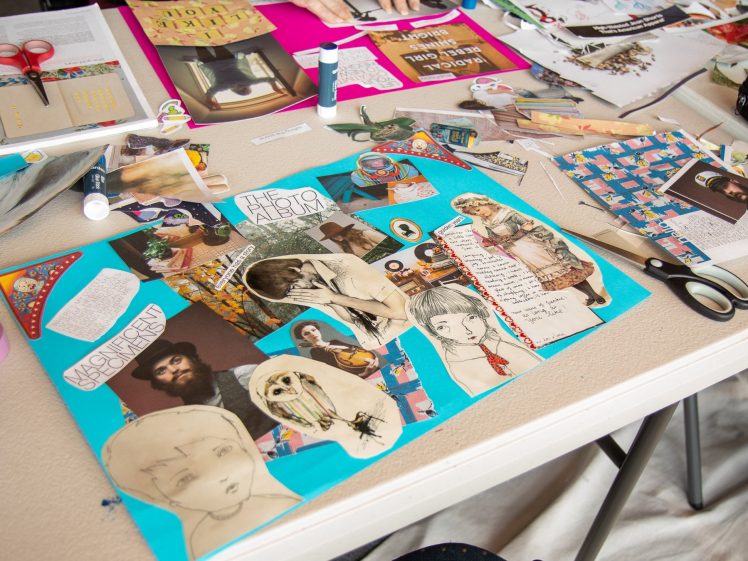 Image of A table covered with art supplies, paper scraps, scissors, and a colourful collage featuring magazine cut-outs of faces, drawings, text, and other images on a bright blue background.