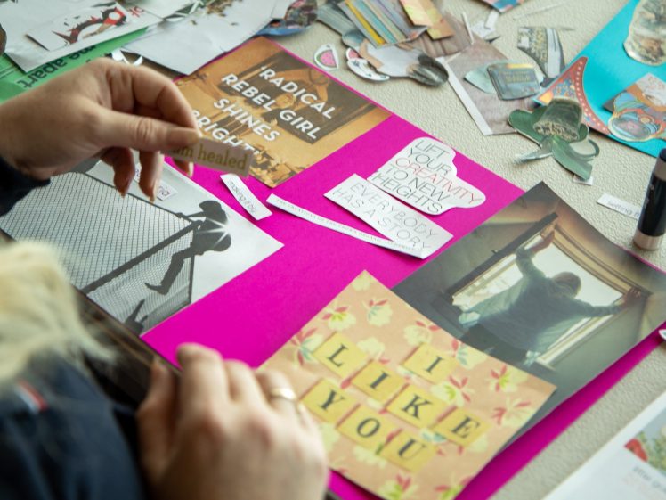 Image of A person arranges cut-out images and motivational phrases, such as Radical rebel girl shines and I like you, on a bright pink poster board during an arts and crafts activity.