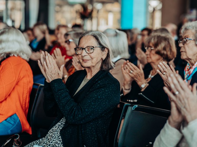 Image of A group of older adults sitting in rows, applauding and attentively watching an event. The atmosphere appears lively, with many people engaged and focused on what is happening in front of them.
