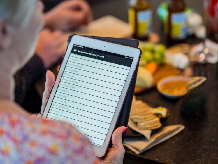 Image of A person holds a tablet displaying a checklist; in the background, there are bottles, food, and snacks on a table, suggesting a social or casual gathering.