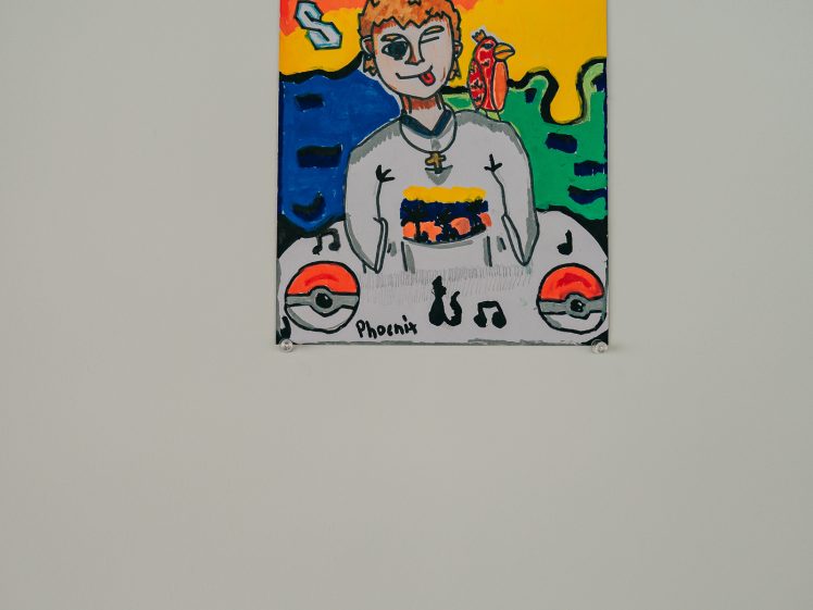 Image of A colourful artwork of a person with a crown, necklace, and parrot, surrounded by vibrant shapes and Poké Balls. Musical notes and the word Phoenix appear at the bottom. The painting is displayed on a white wall.