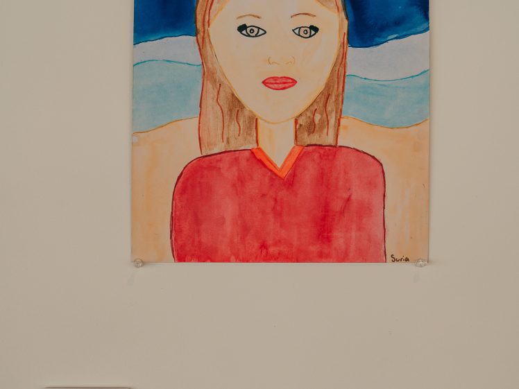 Image of A colourful painting of a woman with long brown hair at the beach, with waves, a turtle, and a starfish in the background. The painting is mounted on a wall with a small label beneath it.