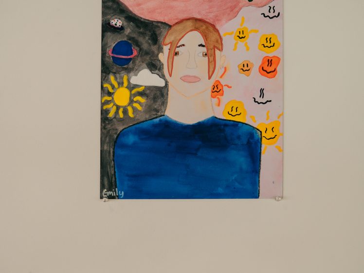 Image of A colourful painting of a person with brown hair wearing a blue shirt, surrounded by sun, planets, and smiley faces, with a background of pink sky and tree branches with flowers. An artist label is displayed below the artwork.