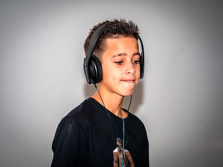 Image of A boy wearing black headphones and a black T-shirt listens intently, looking slightly down and biting his lower lip, against a plain white background.