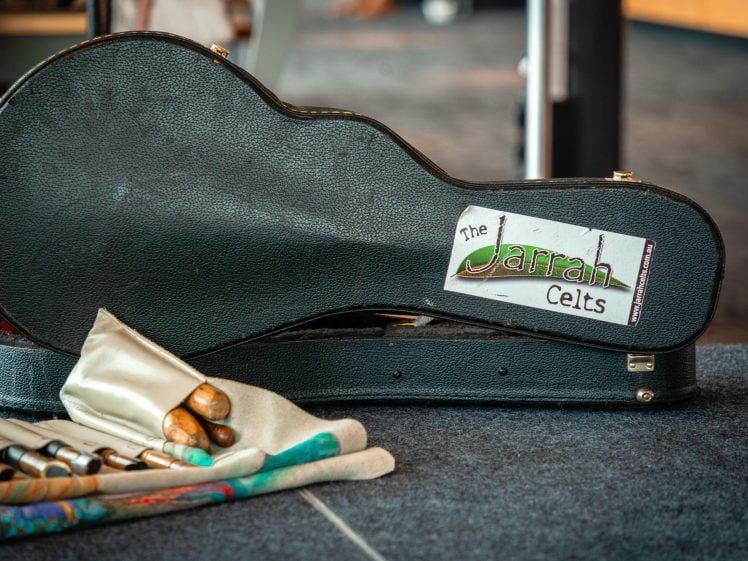 Image of A black instrument case with a sticker reading The Jarrah Celts rests on the floor next to a cloth pouch holding several wooden-handled tools or instruments.