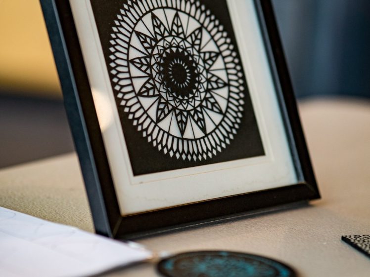 Image of A framed black and white geometric mandala artwork sits on a table, surrounded by round coasters with similar intricate patterns.