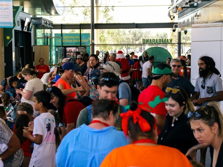 Image of A busy indoor event with many people, including children and adults, some wearing festive hats and fancy dress. The crowd appears to be enjoying a holiday celebration in a bright, modern space.