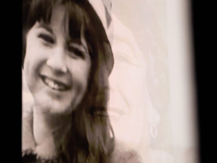 Image of A photograph showing a black-and-white double exposure of a young girl smiling in the foreground and an older woman’s face faintly visible in the background. Both wear coats and hats, suggesting different generations.