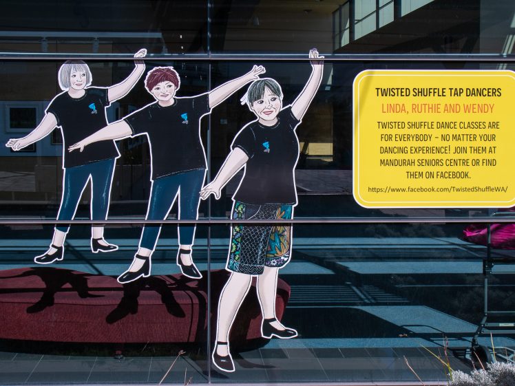 Image of A window display shows three illustrated women tap dancing, all smiling and raising their arms. Beside them is a yellow sign promoting Twisted Shuffle Tap Dancers and their Facebook page, inviting people to join dance classes.