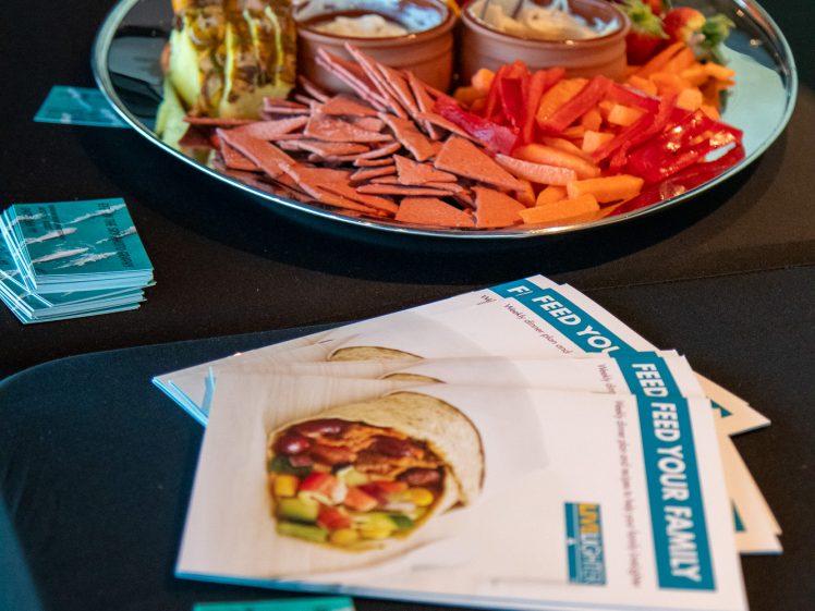 Image of A platter of sliced cooked meats, vegetables, fruit, and dipping sauces sits on a black table next to informational leaflets and a stack of business cards.