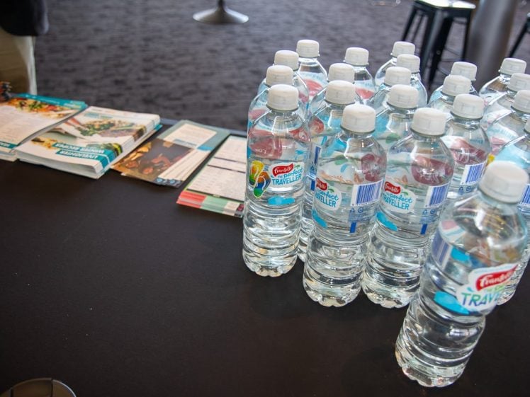 Image of Several bottles of water are arranged on a black table next to a stack of leaflets, brochures, and open magazines in an indoor setting.