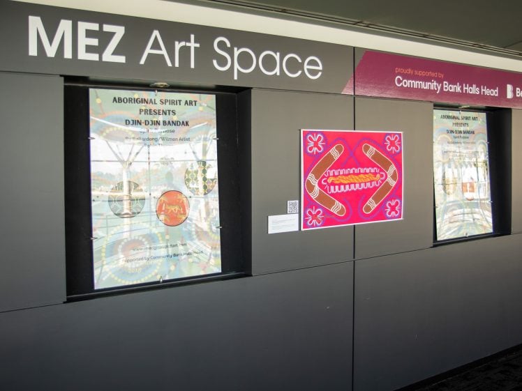 Image of The MEZ Art Space wall features two windows with posters for Aboriginal Spirit Art Presents Djin Djin Bamba and a vibrant pink artwork with Indigenous patterns displayed between them.