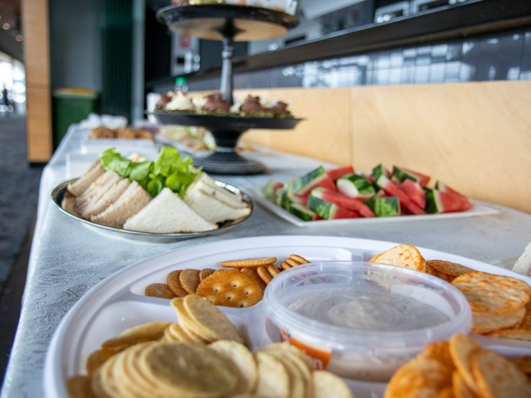 Image of A close-up of a platter with assorted crackers and dip, with trays of finger sandwiches and sliced watermelon in the background on a buffet table.