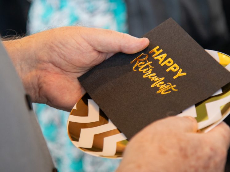 Image of A person holds a chevron-patterned plate and a black card with gold lettering that says Happy Retirement.