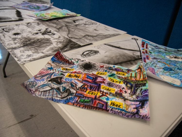 Image of A table displays several colourful and black-and-white art pieces, including one with vibrant scribbles and labels, and others with abstract drawings and sketches, all laid out on a white surface.