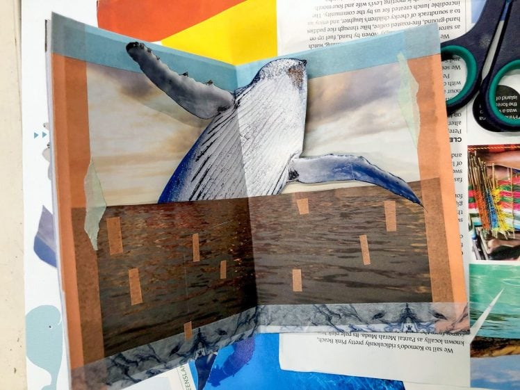 Image of A handmade collage featuring a breaching whale above an ocean, with brown rectangular shapes over the water, bordered by coloured tape. Craft materials, scissors, and papers are scattered around the artwork.