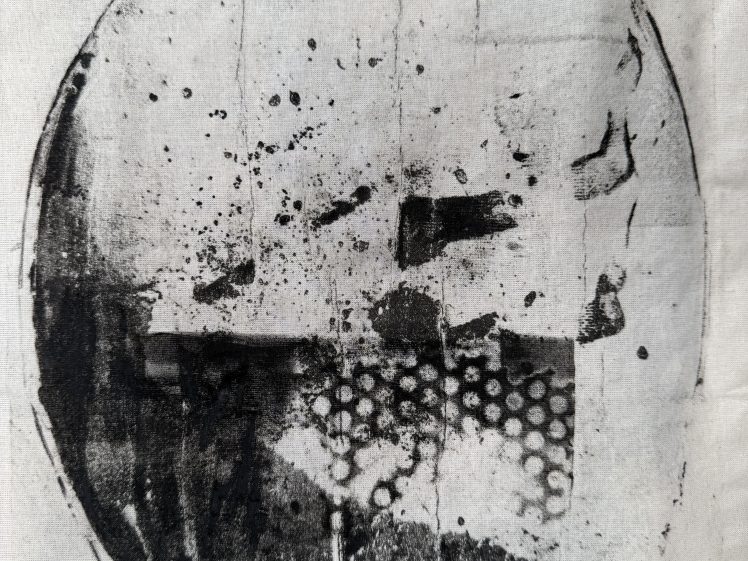 Image of Black and white abstract circular print with irregular shapes, splatters, lines, and a cluster of small dots in the lower half, all set against a light background.